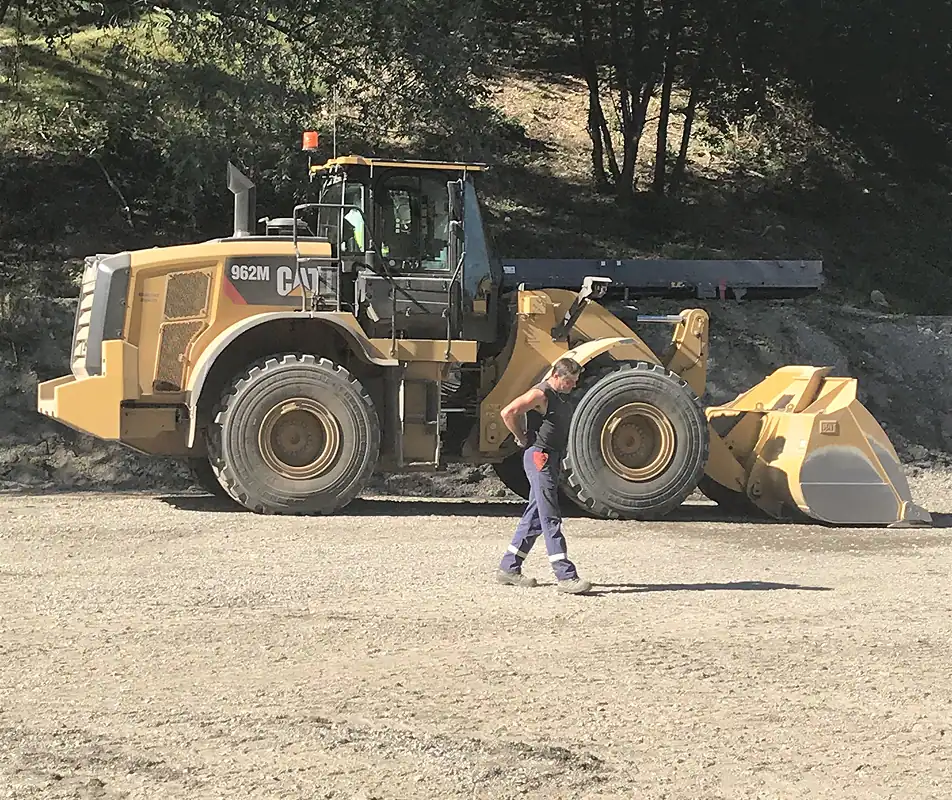 Technicien Ecograv marchant devant une chargeuse sur pneus CAT 962M sur chantier de terrassement - équipe qualifiée BTP recyclage