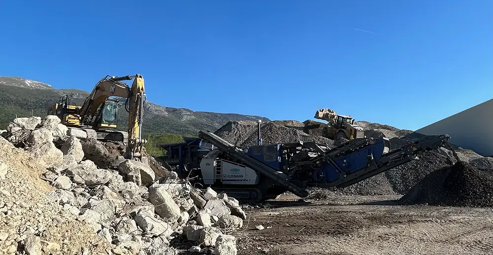 Pelle CAT et concasseur mobile Ecograv sur chantier de concassage de gros blocs rocheux en montagne - recyclage matériaux BTP